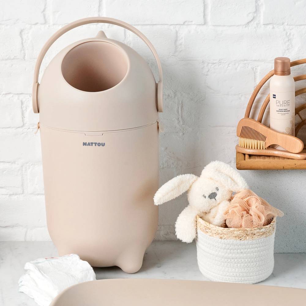 Beige nappy bin with a toy and basket on a white surface.