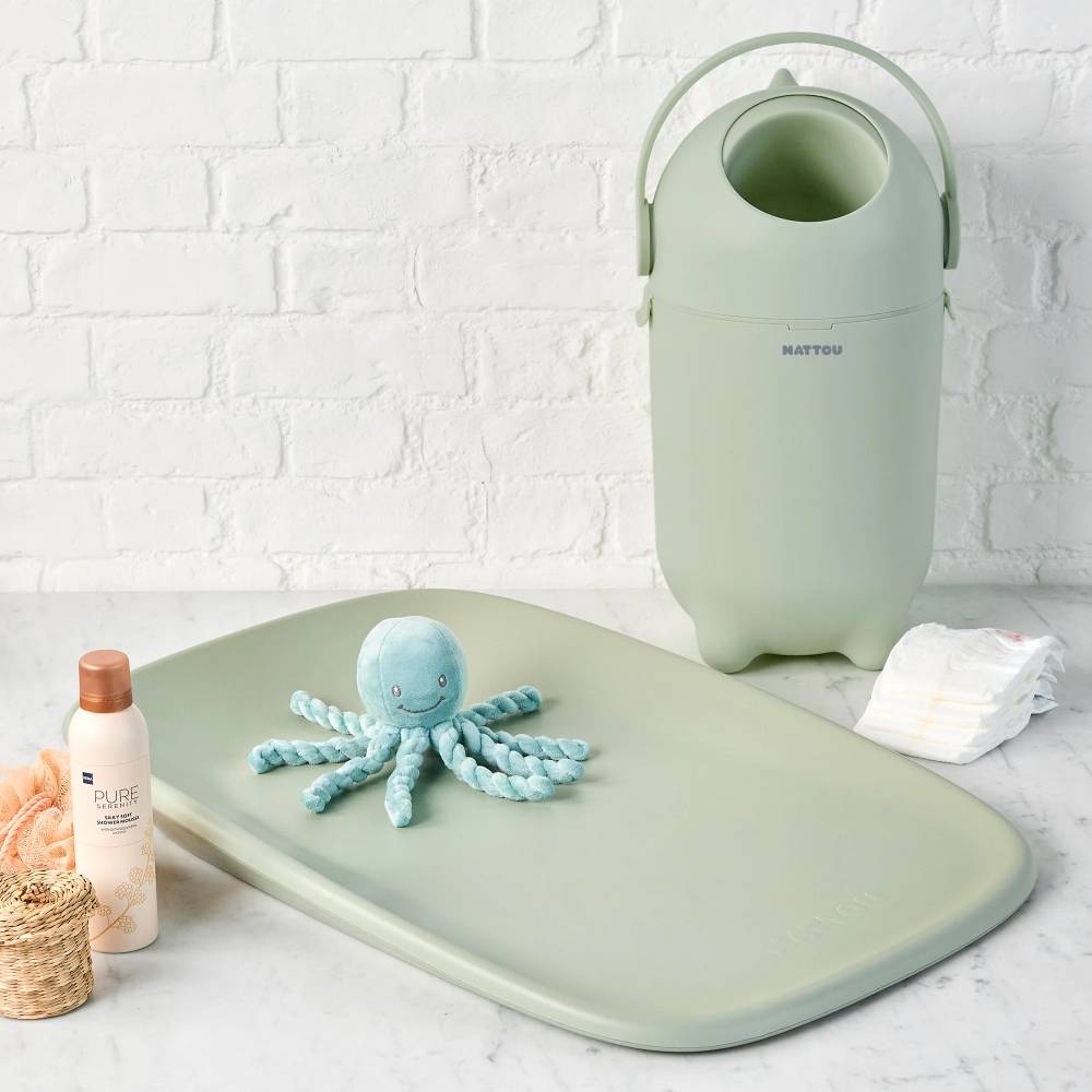 Sage green nappy bin with sage green change table and toy octopus, bottle, and bucket on a white surface.