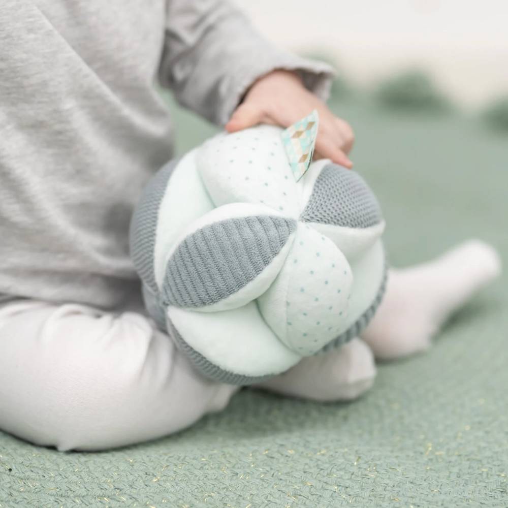 Child holding a soft, textured ball toy on a green surface