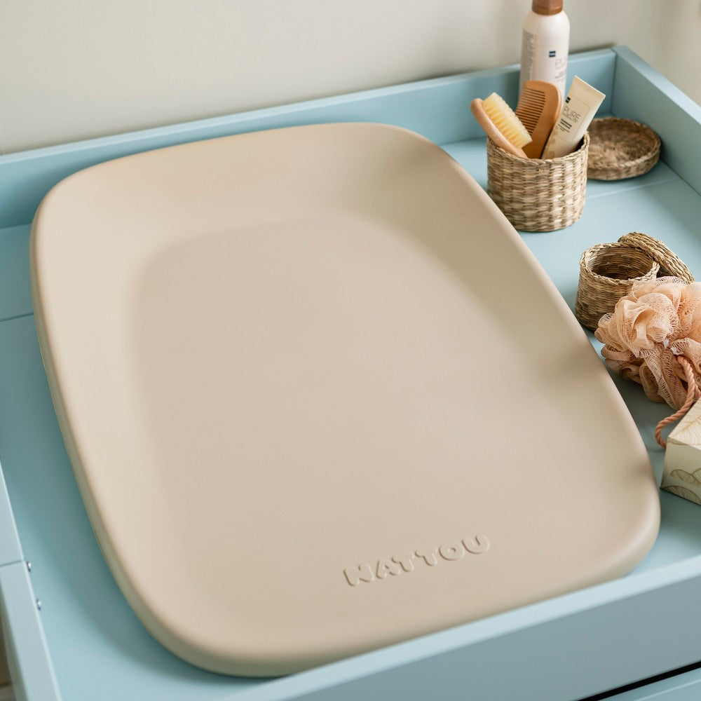 Beige change table for baby with 'NATTOU' branding on a light blue surface with decorative items.