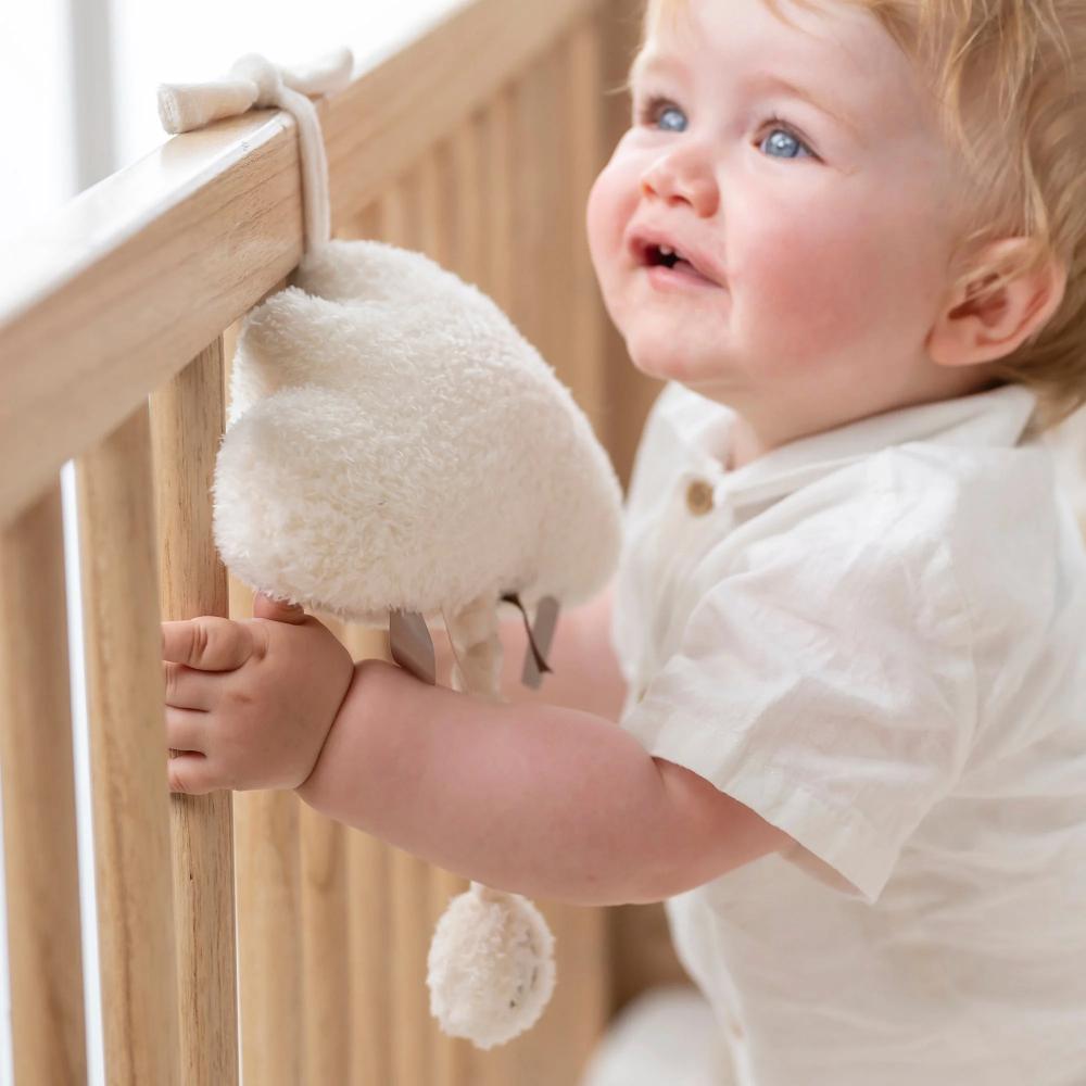 Baby in a crib with a soft musical toy hanging from the side