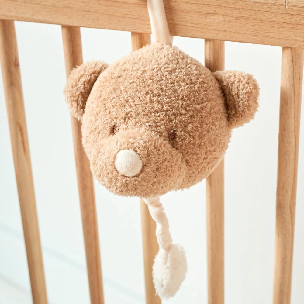 Plush musical teddy bear toy hanging from a crib rail with a light background