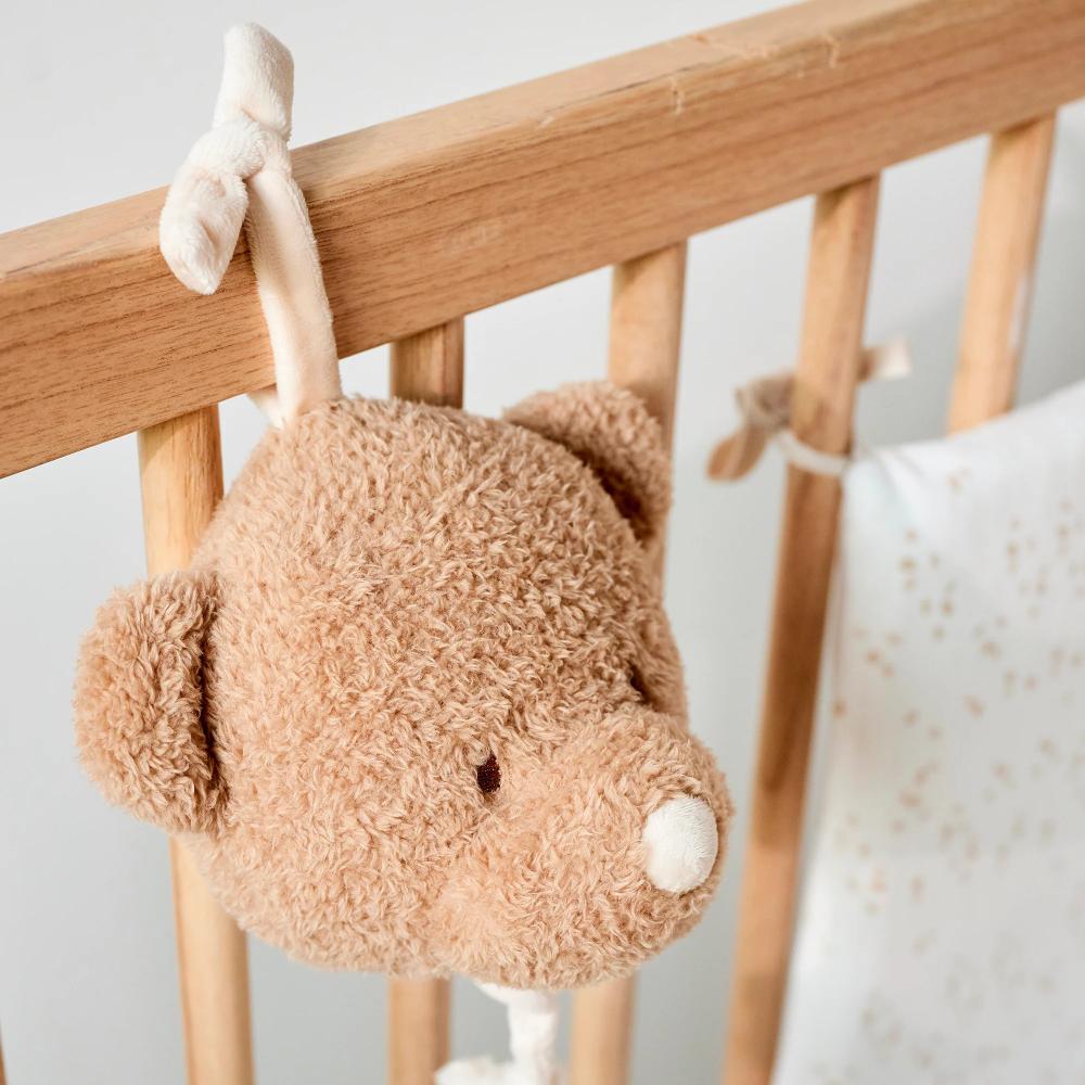 Plush musical toy hanging from a crib rail with a neutral background