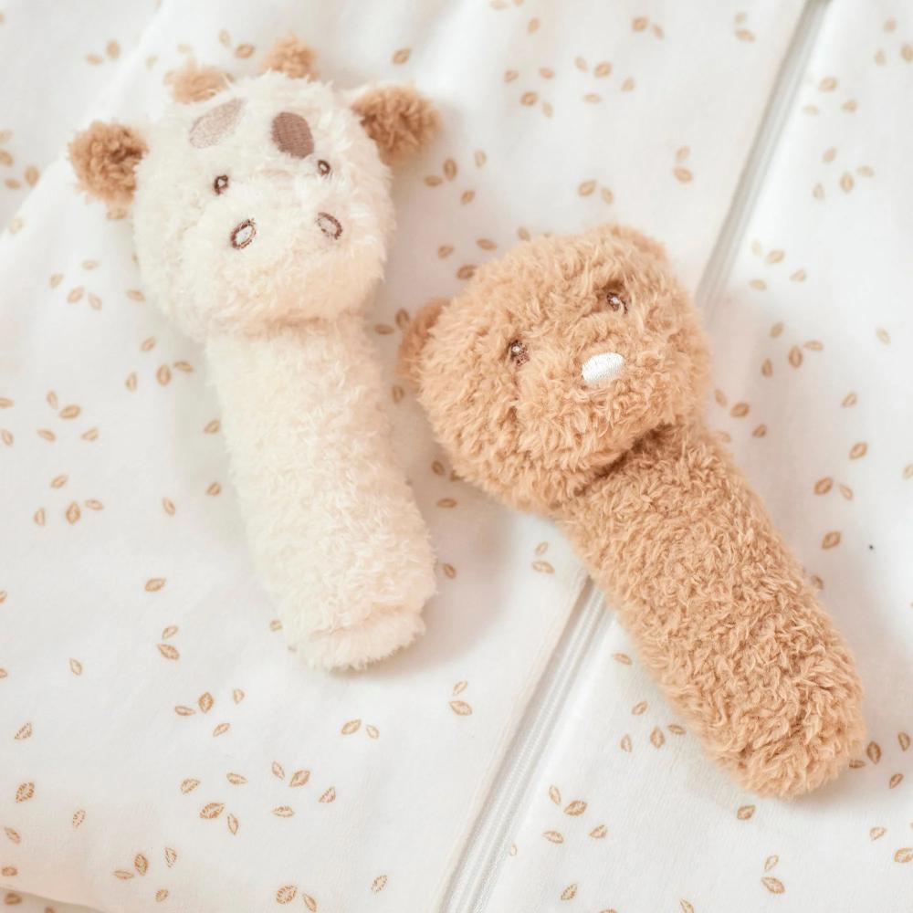 Two plush toy rattles, one white and one brown, on a textured surface.