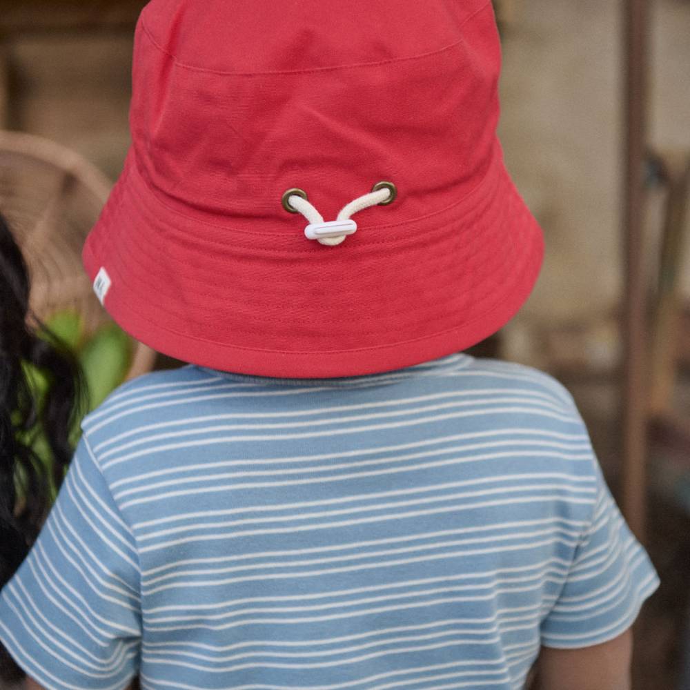 The back view of a child wearing a red bucket hat with a blue stripe tee. 