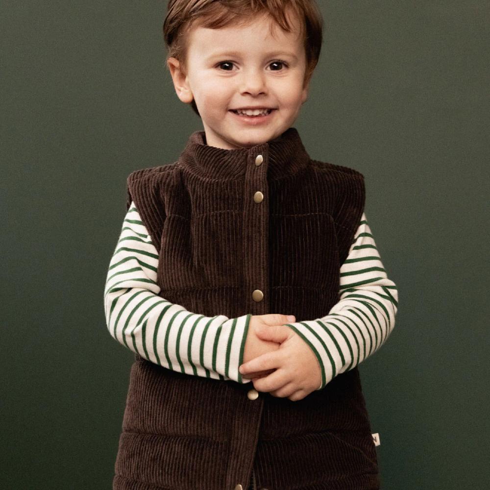 Child wearing a brown vest over a green and white striped cotton shirt against a green background