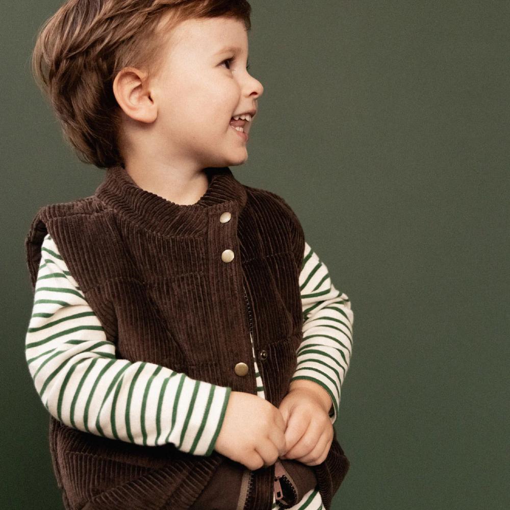 Child wearing a brown corduroy vest over a green and white striped shirt against a green background