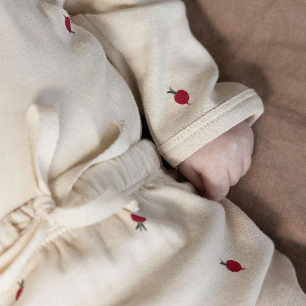 Close up of a baby in cream outfit with red radish patterns lying on a brown surface