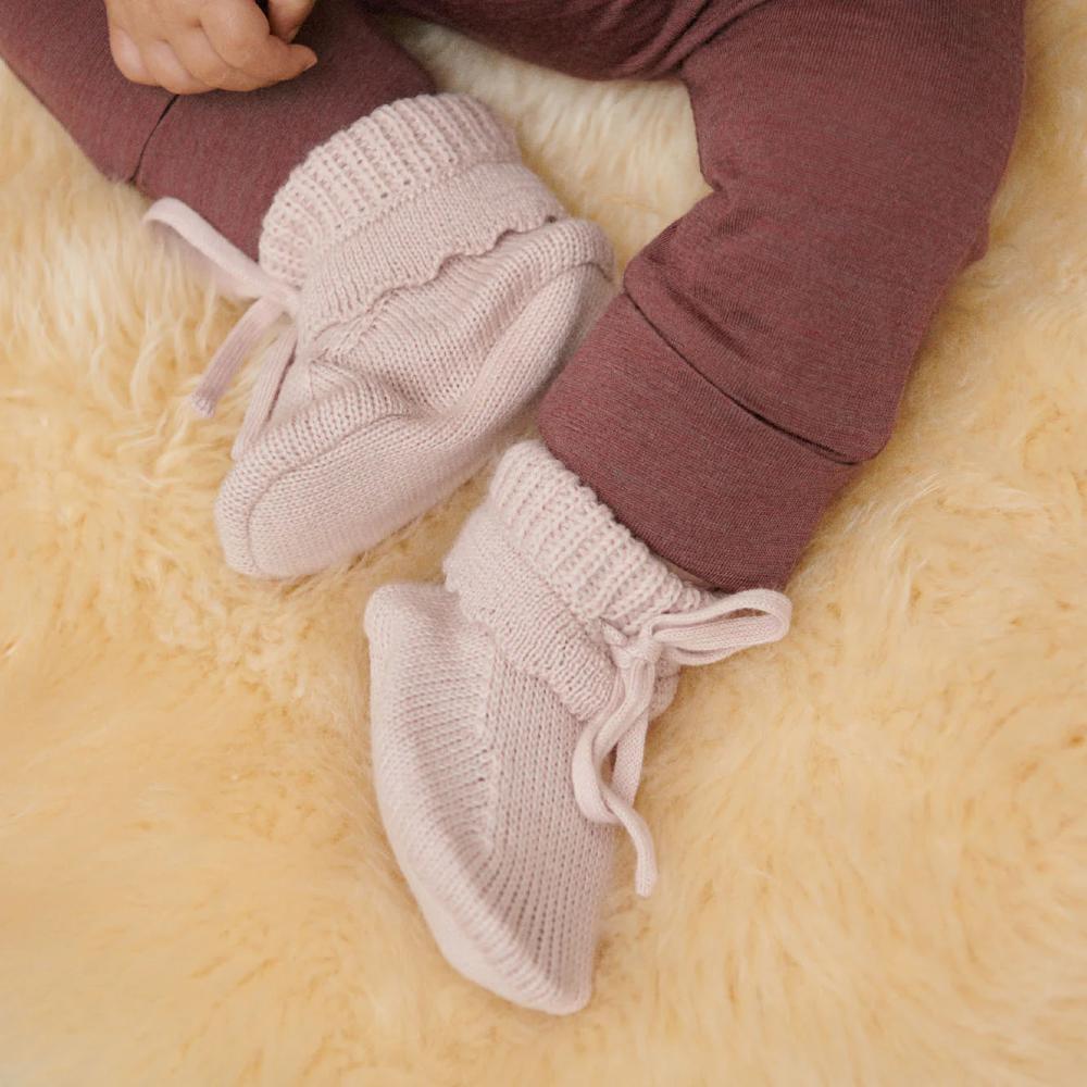 Close-up of a baby's feet wearing pink knitted booties on a soft yellow woolen surface