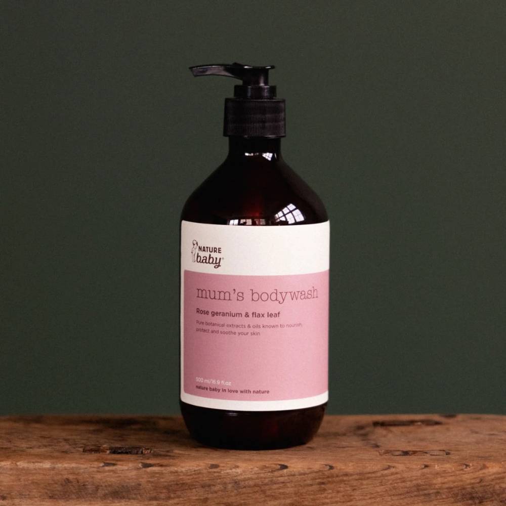 Bottle of 'Nature Baby' mum's bodywash with pink and white sticker and black pump on a wooden surface with a dark green background