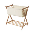 Wooden baby bassinet with crossed ends with beige fabric cover on a white background