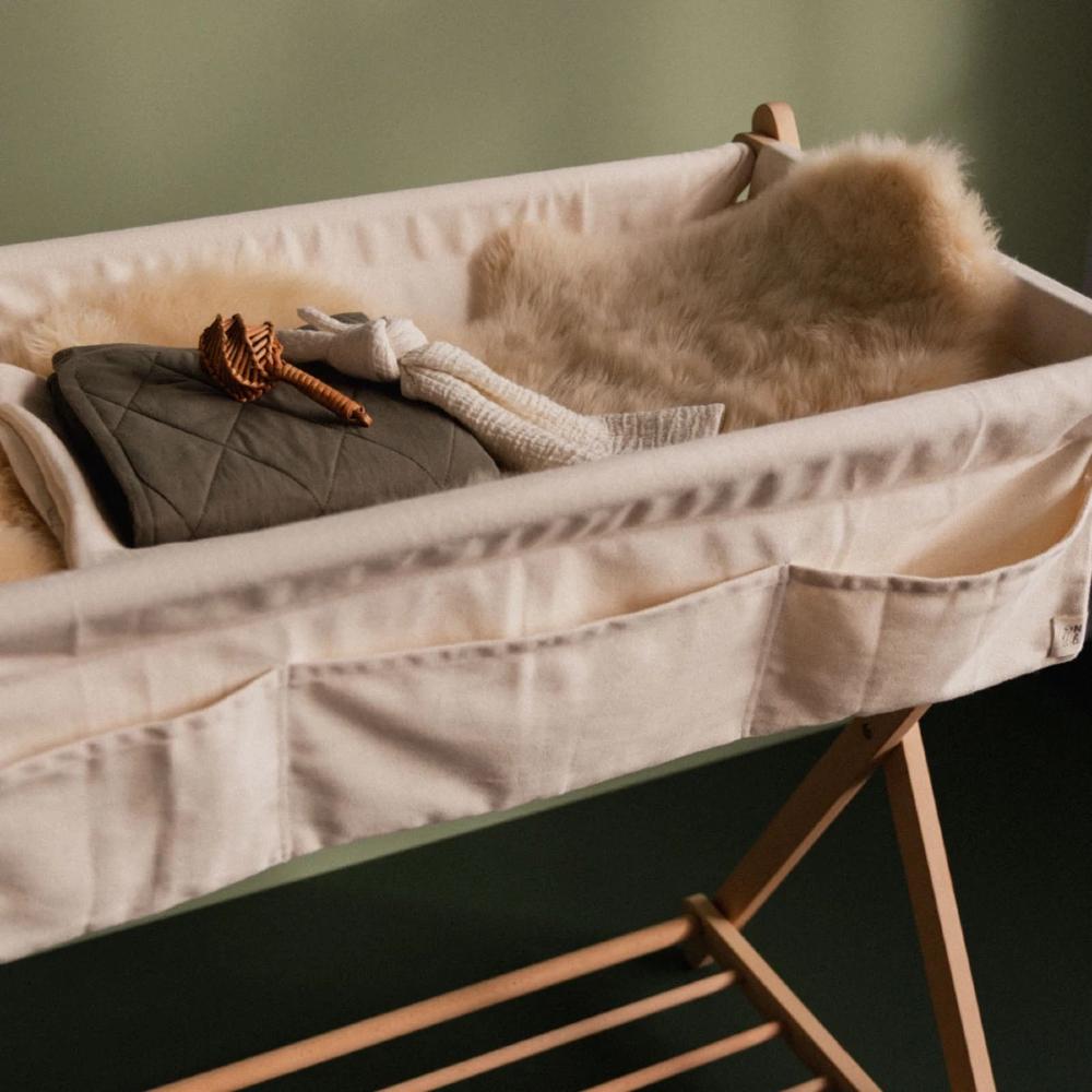 Cream coloured cotton change table with soft bedding and toys against a green background