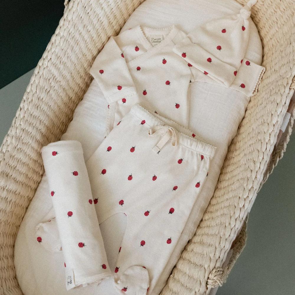 Cream Baby outfit with red raspberry pattern with matching hat and blanket in a wicker moses basket