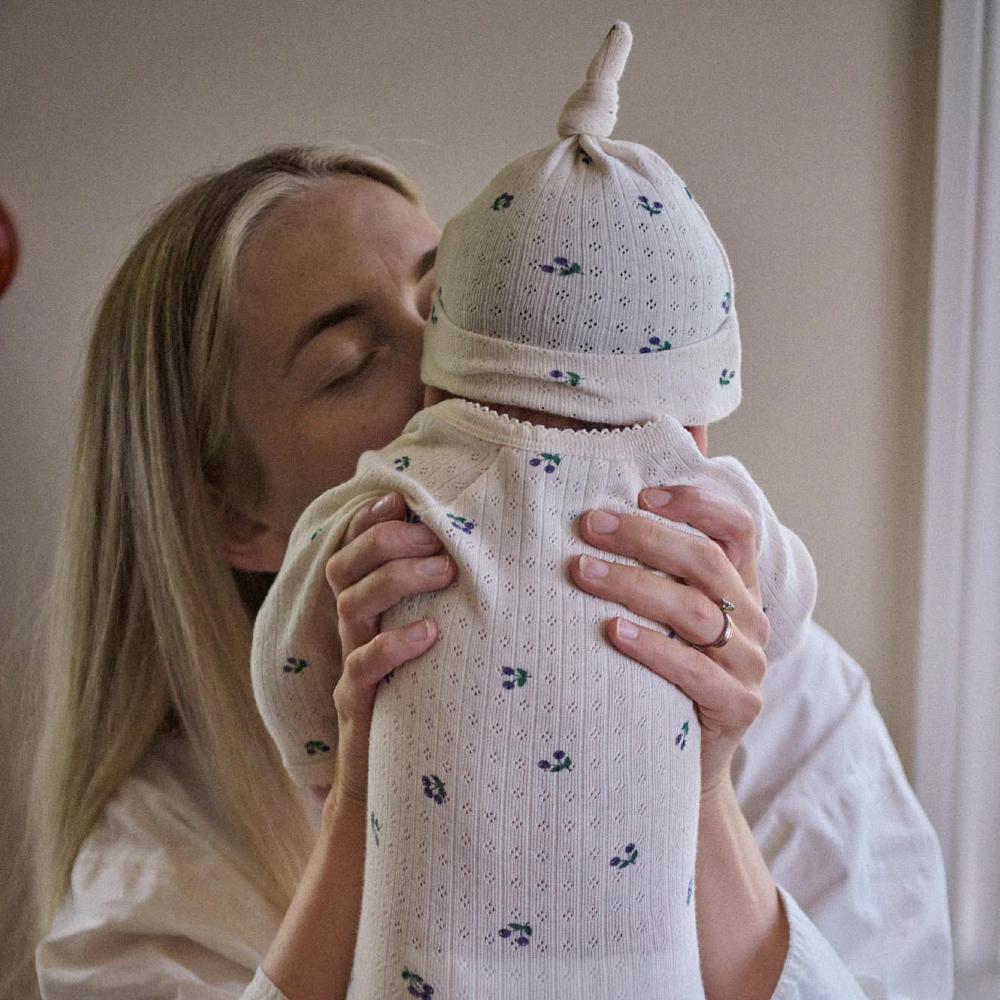 Woman holding a baby wearing a white pointelle bodysuit with purple berry pattern and matching hat