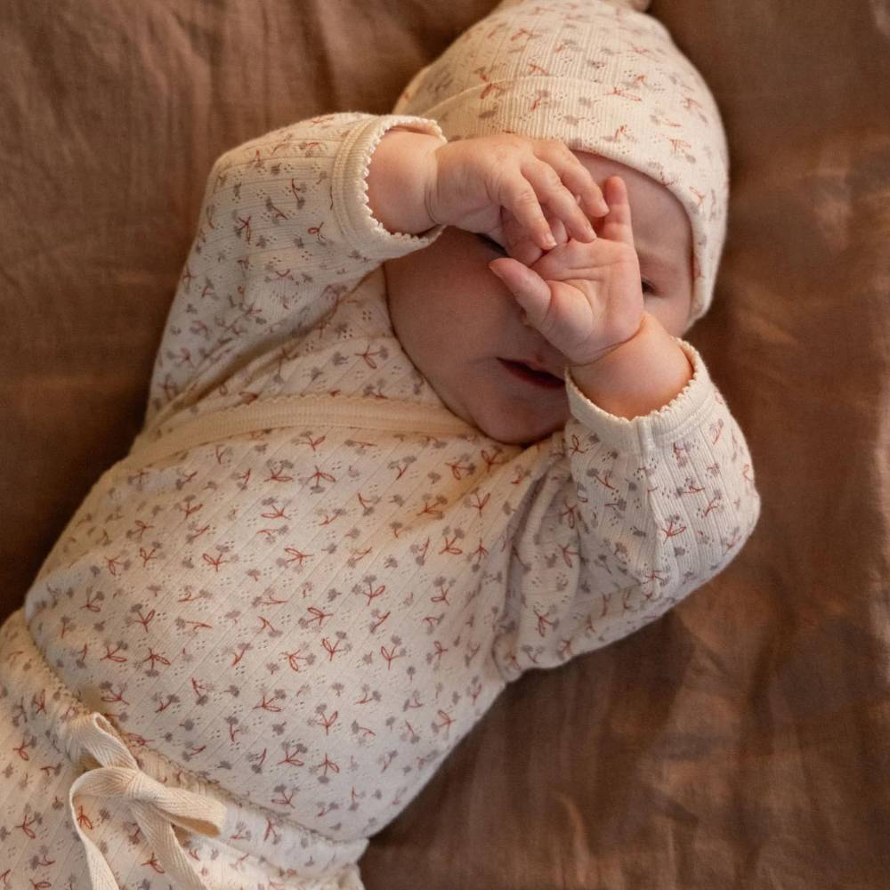 A baby lying down wearing floral macthing oufit - long sleeve bodysuit, leggings and a knotted beanie. 