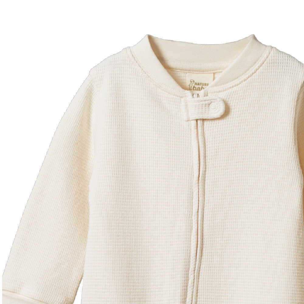 Close-up of an organic cotton waffle texture cream-colored baby onesie with a zipper on a white background