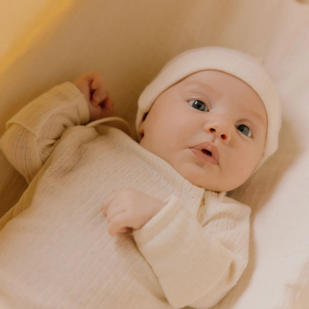Baby in a cream merino pointelle baby gown outfit lying on a soft surface