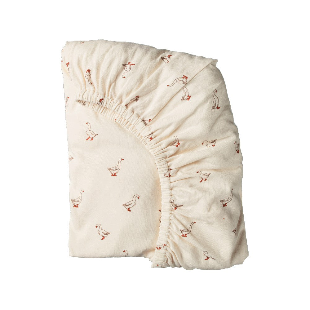 An off-white organic cotton fitted sheet with a delicate red and brown goose pattern, shown folded on a solid white background.