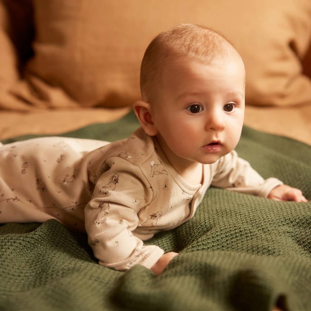 Baby lying on a green merino wool knitted blanket with a soft brown background