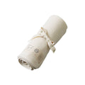 Rolled-up cream pointelle merino wool fabric with a nature baby brand label and tie on a white background