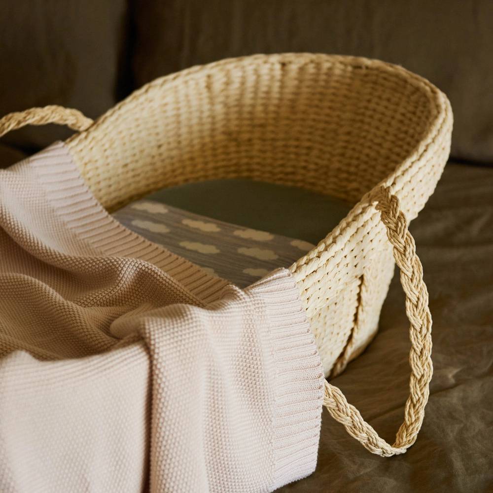 Beige Woven moses basket with a beige blanket inside on a brown surface