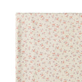 A close-up of a swaddle wrap with a delicate repeating floral pattern on a warm off-white background.