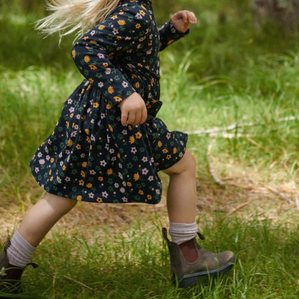 Child in a navy floral dress and boots with lilac cotton rib socks walking on grass