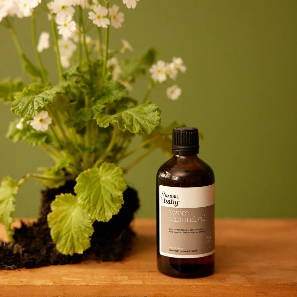 Brown bottle of sweet almond oil with a brown and white sticker and nature baby branding wooden surface with a plant in the background