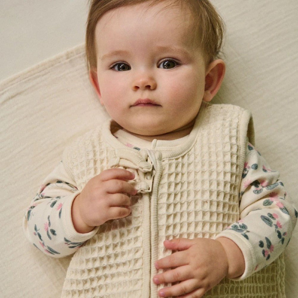 Baby wearing a textured waffle beige sleeping bag against a neutral background