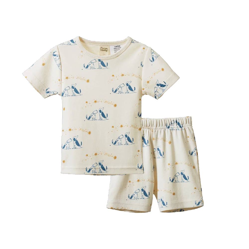 A two-piece pajama set featuring a short-sleeve top and matching shorts in cream with a blue dog and yellow star pattern, displayed on a clean white background.