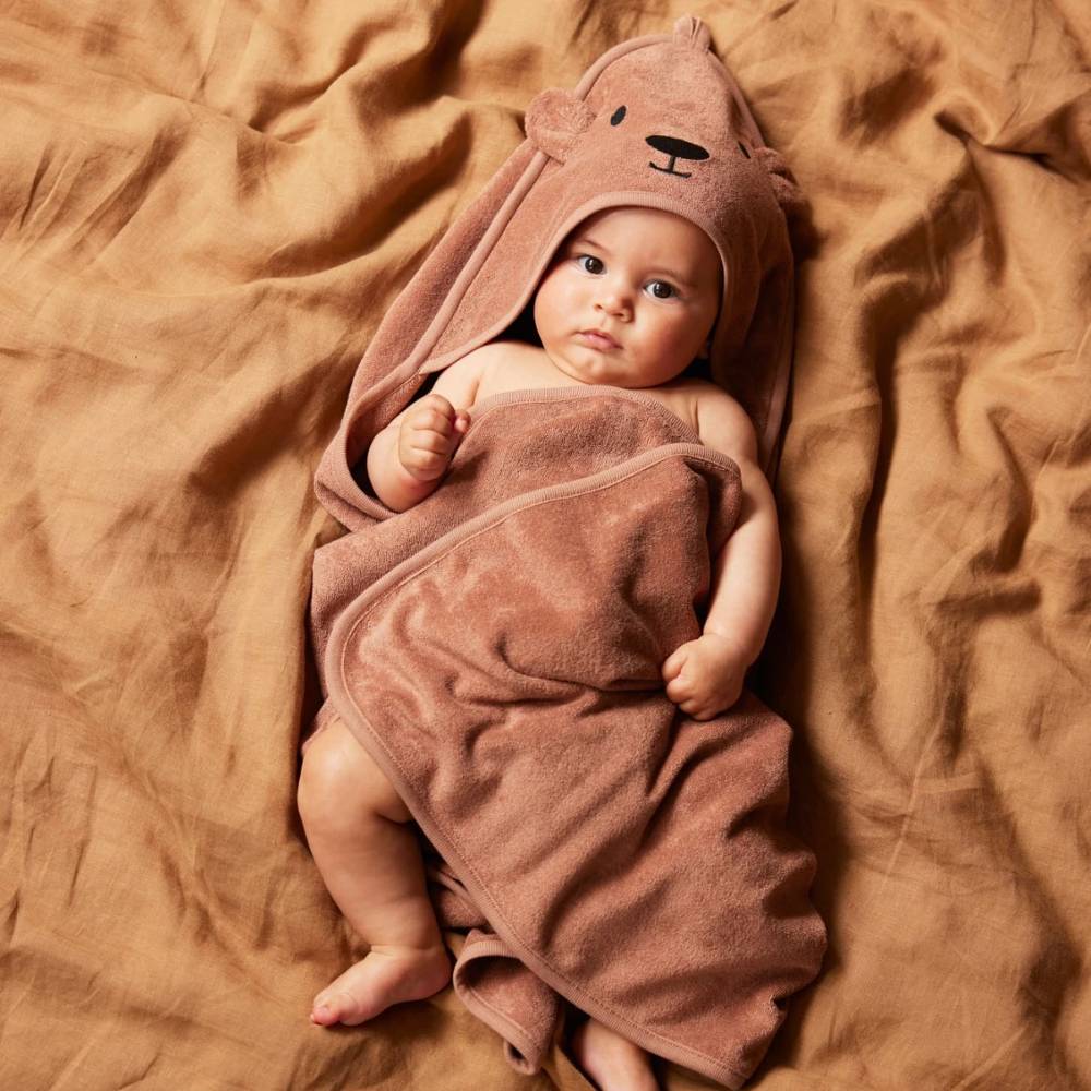 Baby wrapped in a brown terry cotton towel with bear ears on a brown blanket