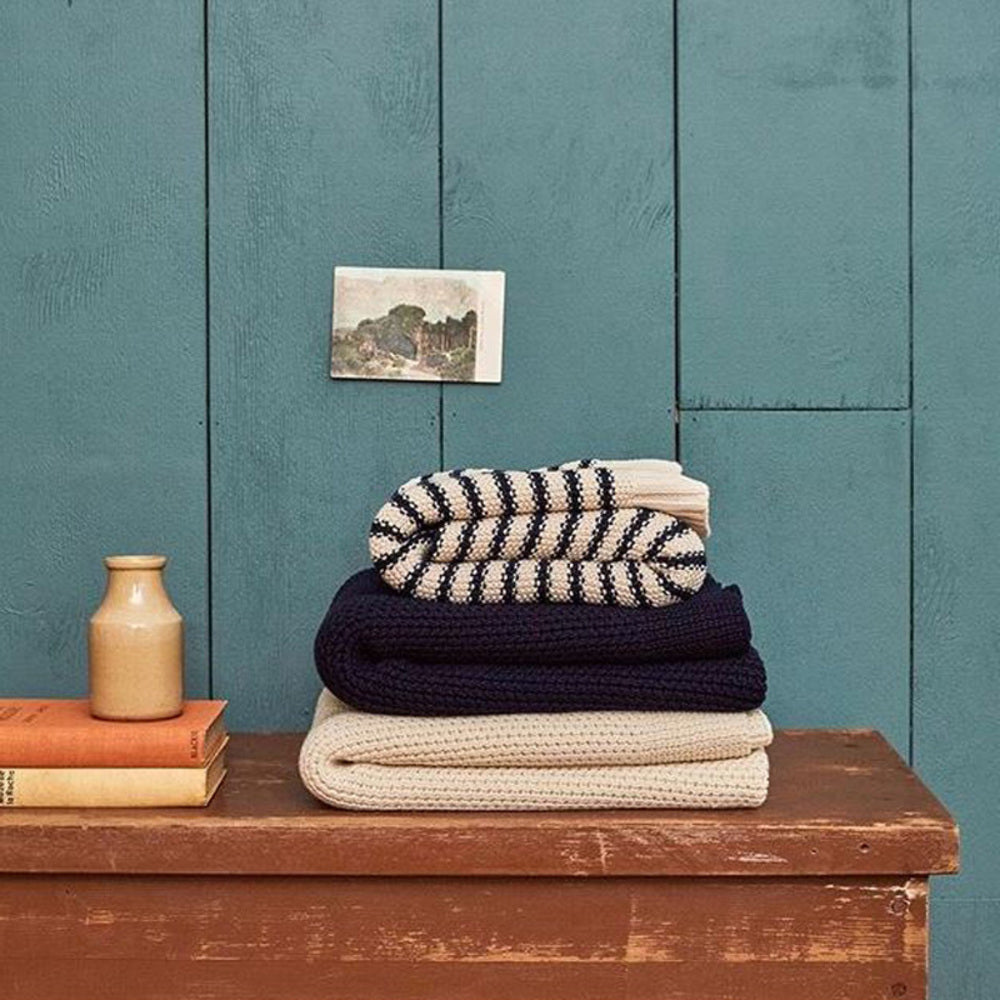 Stack of woolen knitted folded blankets on a wooden surface with a teal wall in the background