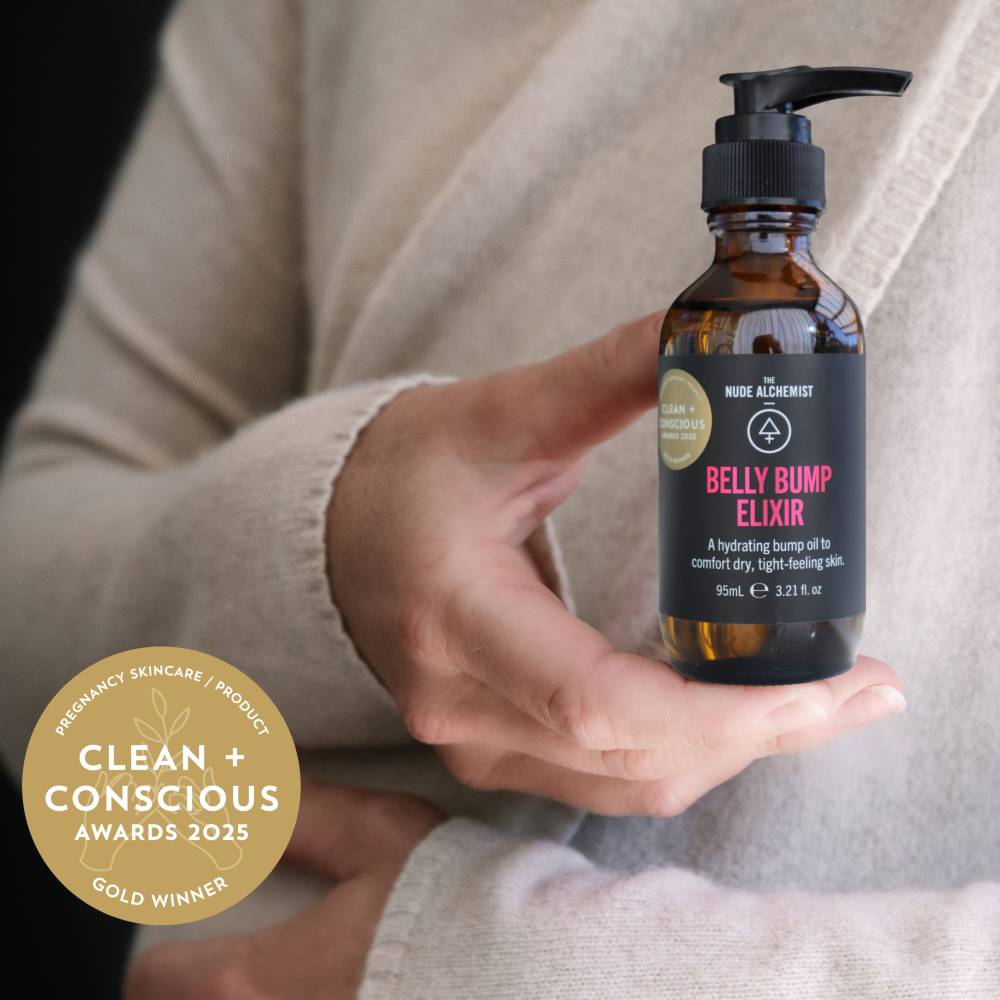 A person in a beige cardigan holds a pump bottle of belly balm oil. 