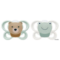 Two baby pacifiers on a white background: one with a bear face in tan and brown with a mint green shield, and one with a smiling frog face in pale green with a white shield. Small text reads 6-4 months.