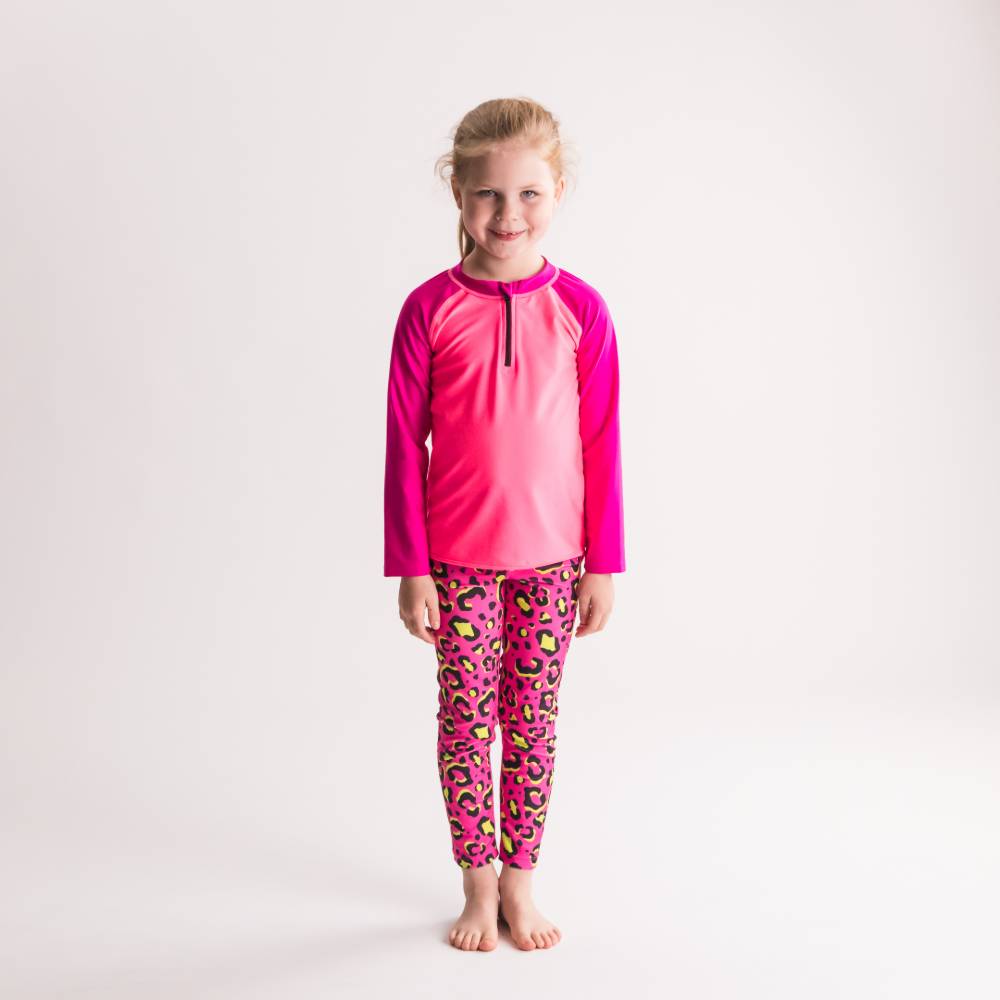 Child wearing a pink long-sleeve rash guard and leopard print pants on a white background