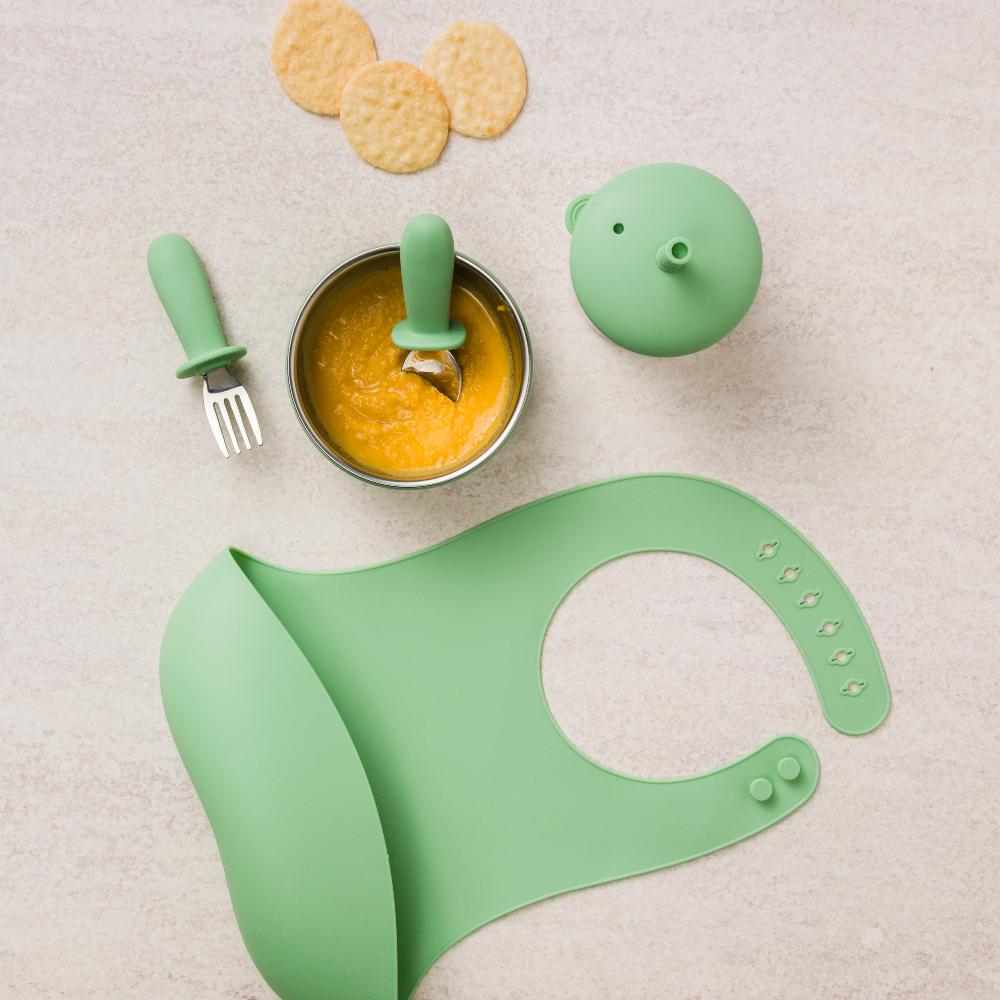 Sage green Nestling baby feeding set with bowl, spoon, fork, and bib on a light background