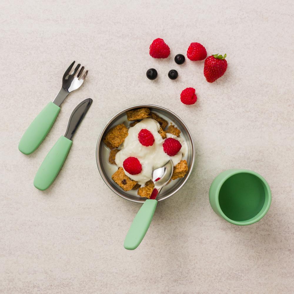 Children's Nestling tableware set with a stainless steel bowl, fork, knife, and cup on a light surface.