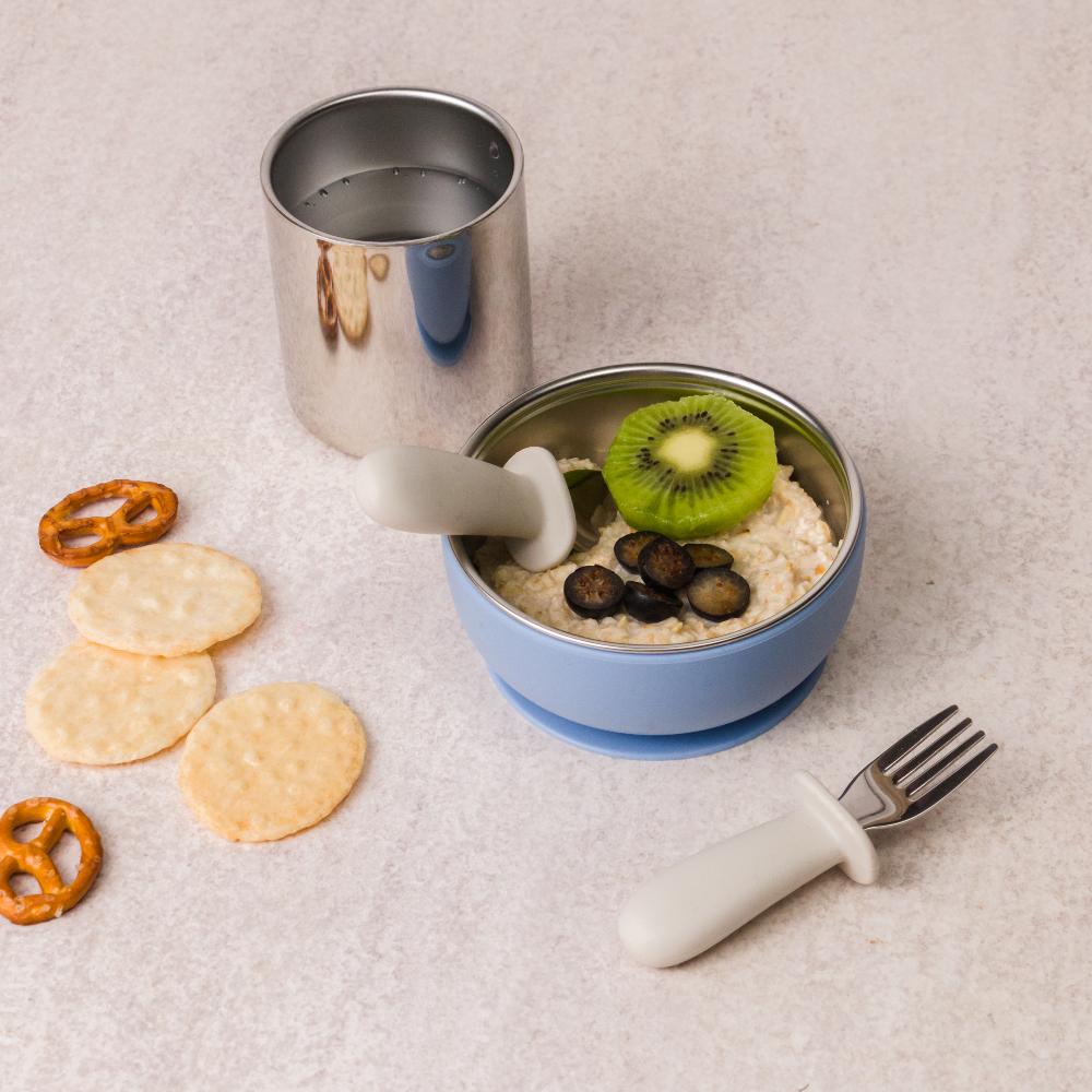 Nestling children's lunch set with stainless steel bowl, cup, and utensils on a light surface