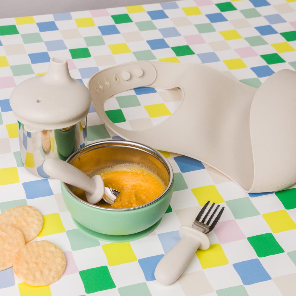 Nestling stainless steel tableware set with bowl, spoon, and fork on a colorful checkered tablecloth.