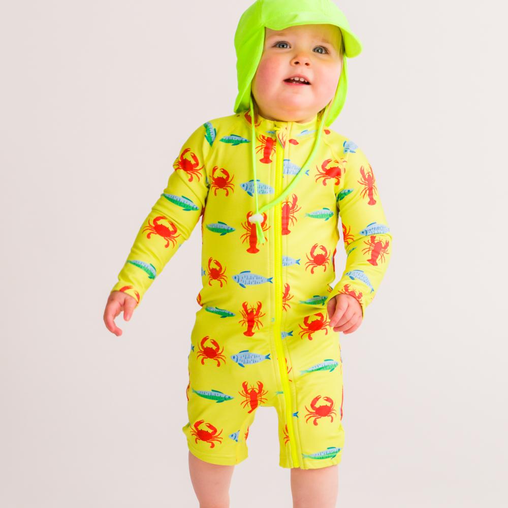 Child wearing a bright yellow swim suit with lobster patterns on a plain background