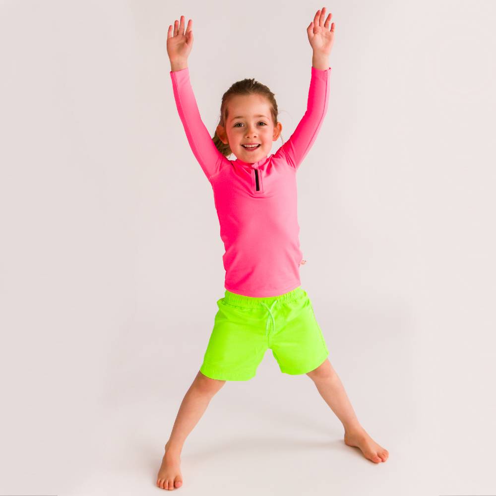 Child wearing a pink long-sleeve rash top and green shorts on a white background