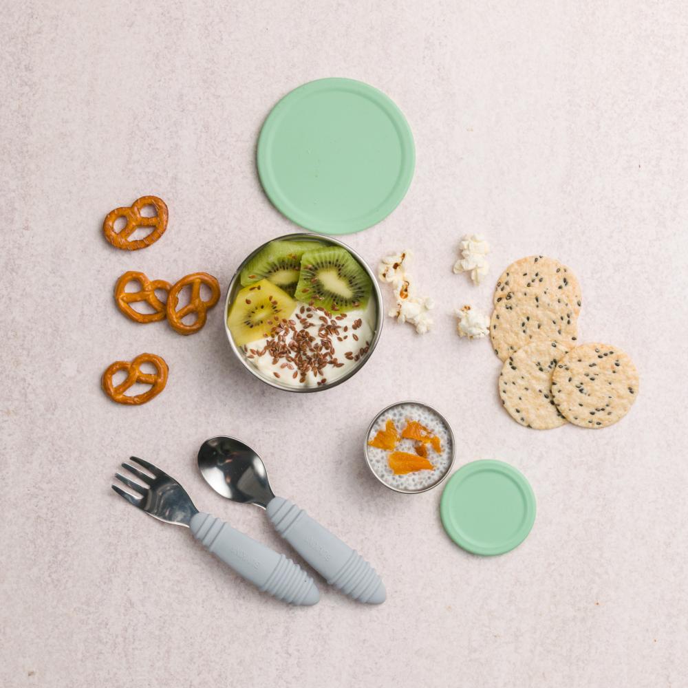 Children's tableware set with bowls, cutlery, and snacks on a light surface