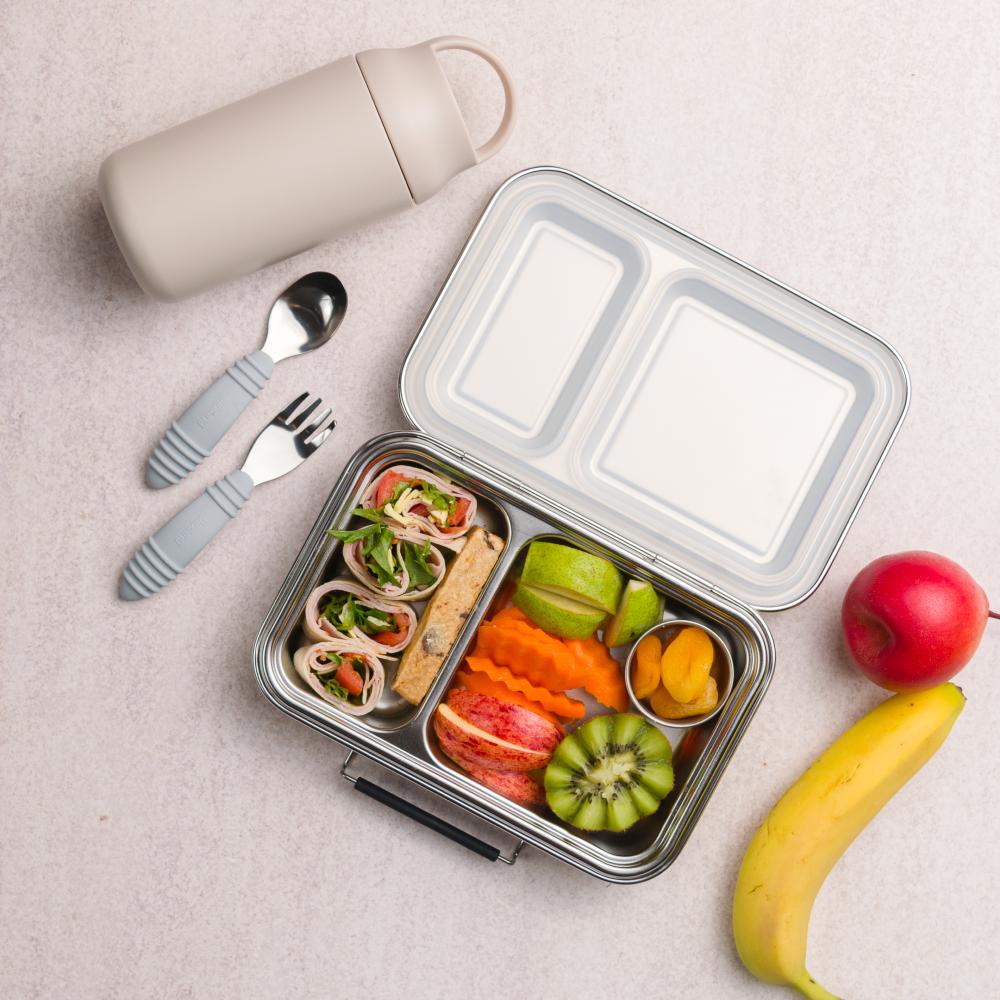 Bento box with compartments filled with food, including fruits and vegetables, on a light surface.