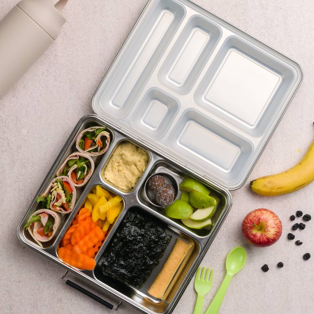 Metal bento box with compartments filled with a variety of food items on a light surface.