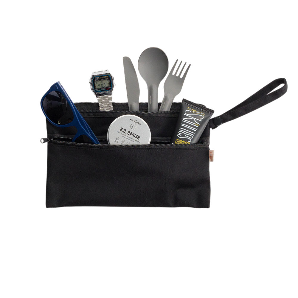 Black travel pouch with utensils, sunglasses, and toiletries on a white background