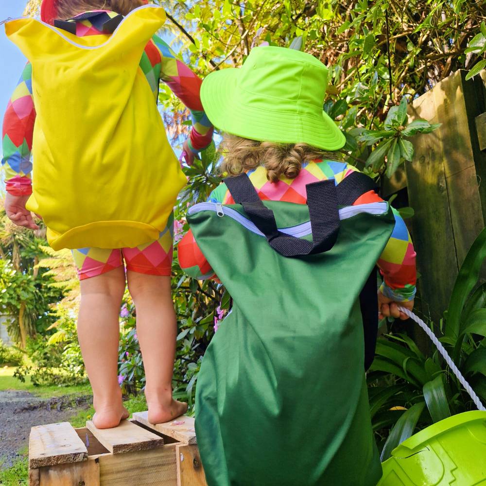 Two children in colorful swim suits and hats standing outdoors with a garden background.