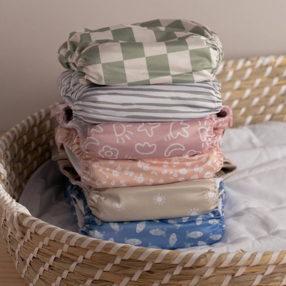 Stack of colorful patterned baby cloth nappies in a woven basket.