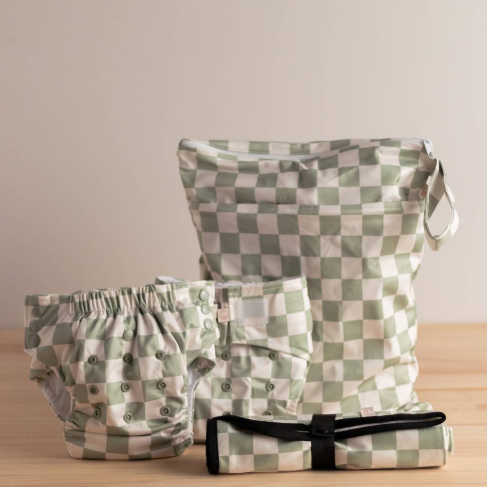 Set of green and white checkered baby clothing and bag on a wooden surface with a beige background