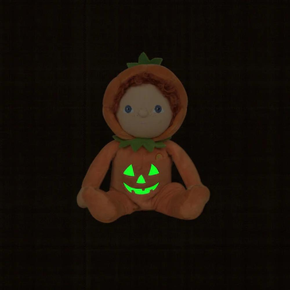 A Halloween-themed plush doll wearing an orange pumpkin costume with a glowing green jack-o'-lantern face on the front, set against a very dark background.