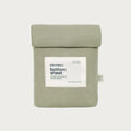 A sage green bottom sheet by babu basics, neatly folded and packaged in a matching fabric sleeve with a white label, set against a light gray background.